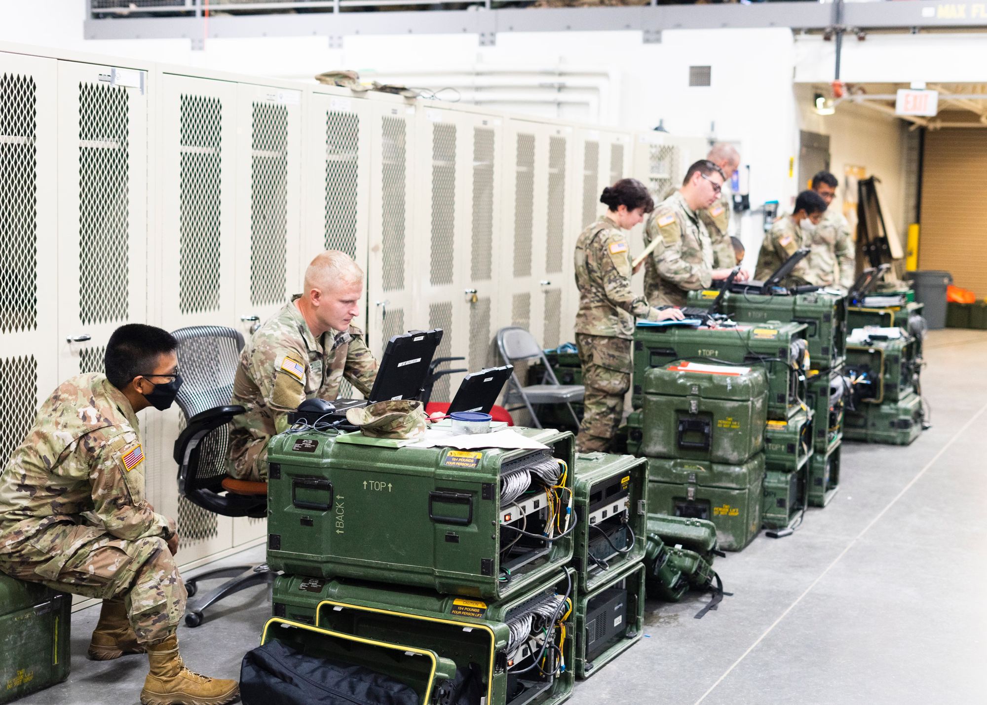Soldiers working on laptops set on transit cases inside a TOC